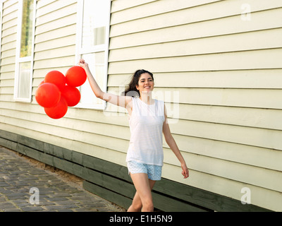 Giovane donna camminando lungo il vicolo con grappolo di palloncini Foto Stock