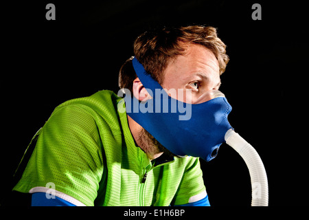 Chiusura del giovane uomo in maschera sulla palestra ciclo di esercizio nel centro di altitudine Foto Stock