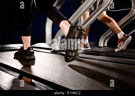 Chiudere fino a maschio e femmina di gambe in esecuzione su palestra Tapis roulant nel centro di altitudine Foto Stock