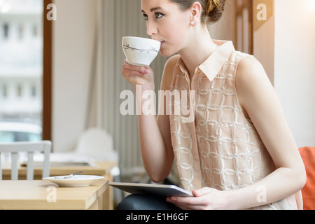 Giovane imprenditrice nel bar a bere caffè e con tavoletta digitale Foto Stock