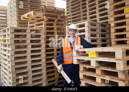 Ritratto di giovane lavoratore di sesso maschile e pile di pallet in legno cantiere Foto Stock