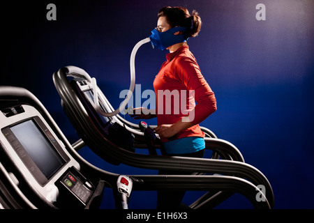Metà donna adulta con maschera facciale in esecuzione su palestra Tapis roulant nel centro di altitudine Foto Stock