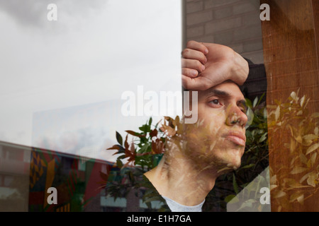 Giovane uomo con la mano sulla testa, guardando attraverso la finestra Foto Stock