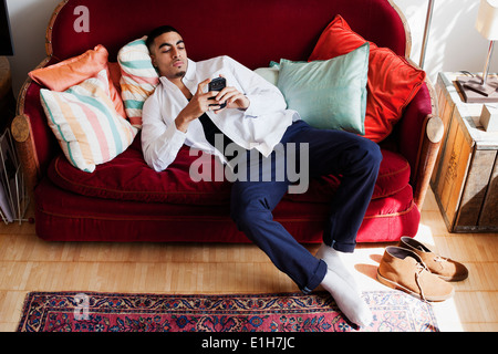 Giovane uomo sdraiato sul divano, utilizza lo smartphone Foto Stock