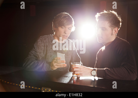 Due amici maschi guardando lo smartphone nel night club Foto Stock