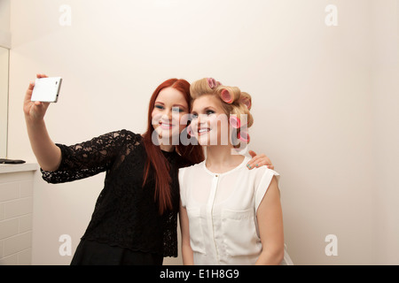 Giovane donna in bigodini e amico tenendo selfie Foto Stock