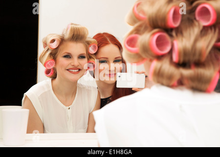 Giovane donna in bigodini e amico tenendo selfie Foto Stock