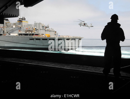 Un U.S. Marinaio a bordo della portaerei USS Nimitz CVN (68) guarda come un MH-60S Knighthawk elicottero assegnato all'elicottero Foto Stock