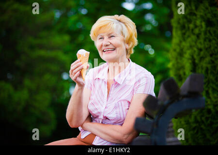 Donna Gray-Haired rilassante con gelateria su banco nel Parco Foto Stock