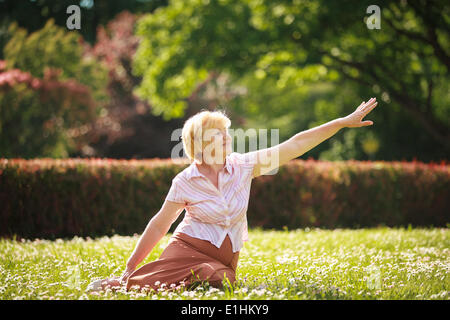 La meditazione. Grazioso vecchia donna nel Parco Stretching la sua mano Foto Stock
