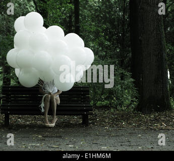 Sentimentalismo. La nostalgia. Lonely donna con aria palloncini seduti sulla panchina del parco Foto Stock