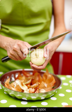 Primo piano delle mani di una giovane donna sbucciare e tagliare la cipolla in cucina Foto Stock