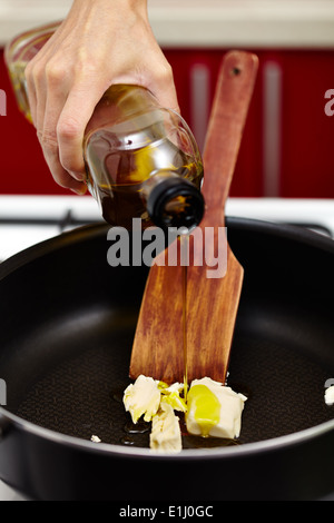 Donna di mano versando olio vergine di oliva su fondere il burro nella padella calda Foto Stock