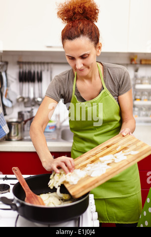 Donna di mettere la cipolla tagliata a fettine in padella Foto Stock