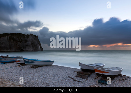 Barche sulla spiaggia di Etretat, Normandia, al tramonto. Porte d'Aval arco naturale in background. Lunga esposizione. Foto Stock