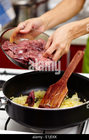 Donna mettendo materie di fegato di pollo in padella con cipolla affettata e condimento Foto Stock