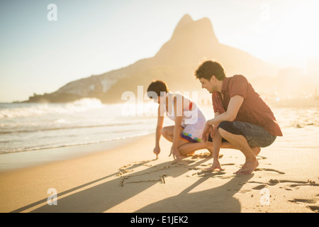 Coppia giovane iscritto sulla sabbia, spiaggia di Ipanema, Rio, Brasile Foto Stock