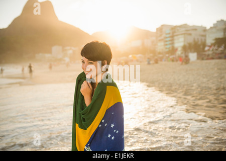 Giovane donna avvolta nella bandiera brasiliana, la spiaggia di Ipanema, Rio, Brasile Foto Stock