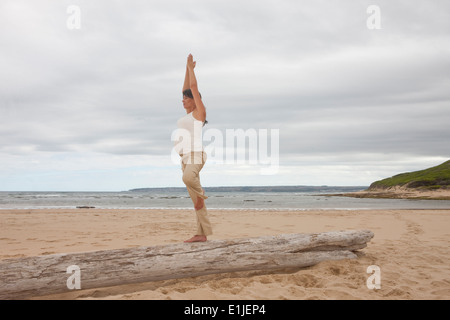 Gravidanza metà donna adulta a praticare yoga sul tronco di albero in spiaggia Foto Stock