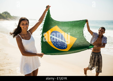 Coppia giovane mantenendo la bandiera brasiliana, Arpoador beach, Rio de Janeiro, Brasile Foto Stock