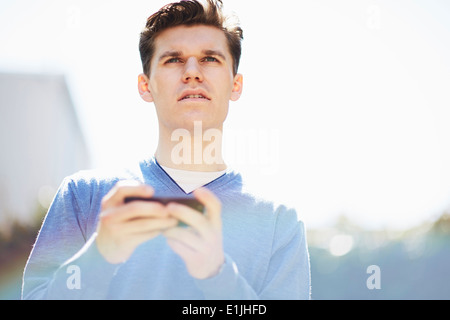 Giovane uomo utilizza lo smartphone, guardando lontano Foto Stock