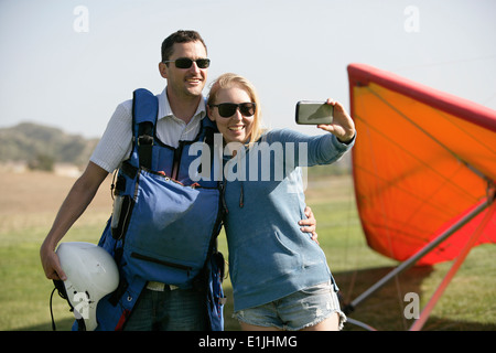 Giovane tenendo selfie, deltaplano in background Foto Stock