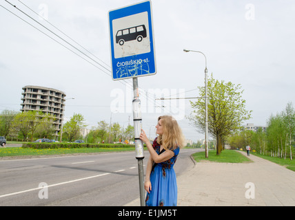 Giovane donna bionda presso la fermata del bus con il bus pole tag programmi di guida Foto Stock