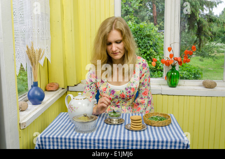 Ragazza preparare erbe balsamo di menta foglie di tè in tazza retrò. A base di erbe della medicina alternativa. Casa rurale veranda decorazioni. Foto Stock