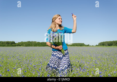 Smile donna pongono nel prato di fiordaliso con bouquet di fiori sul cielo blu sullo sfondo Foto Stock