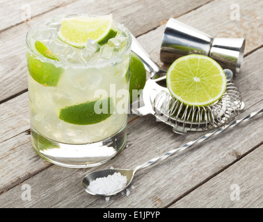 Classico cocktail Margarita con il salato cerchione sulla tavola di legno con tigli e bere utensili Foto Stock