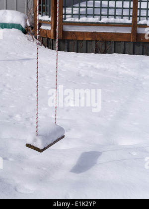 Vuoto coperto di neve Swing. Un bambino impilati a rotazione alta con la neve si blocca in un cortile coperto di neve in una giornata di sole. Foto Stock