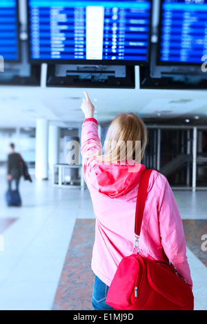 Giovane donna puntando su informazioni di volo in aeroporto. Foto Stock