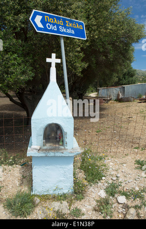 Un santuario sul ciglio della strada si erge di fronte a una strada greca puntando al vecchio Skala, Cefalonia. Foto Stock