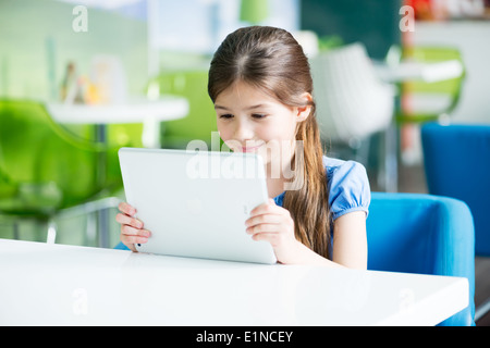 Poco sorridente ragazza seduta alla scrivania e guardando su un marchio nuovo Apple iPad aria Foto Stock