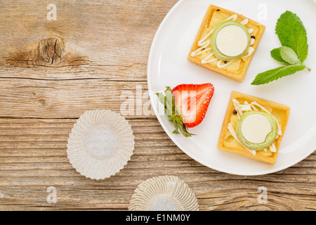 Dessert - crostate con fragola e menta piperita fresca sulla piastra bianca contro la grana di legno stagionato, vista dall'alto Foto Stock