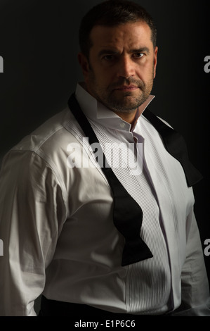 Ritratto a chiave basso di un bel maschio che indossa la camicia e la cravatta ad arco guardando nella fotocamera. Questo è girato con uno sfondo scuro. Foto Stock