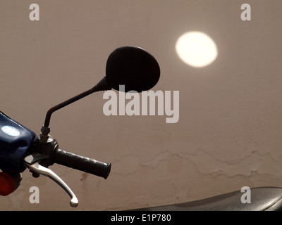 Spotlight di sole riflessa dallo specchio del motociclo sul muro dipinto di bianco altrimenti in ombra Foto Stock