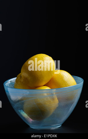 I limoni in una blu ciotola di vetro seduto su un tavolo contro uno sfondo scuro. Foto Stock