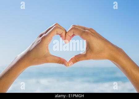 Mani femminili messa a forma di cuore in riva al mare Foto Stock