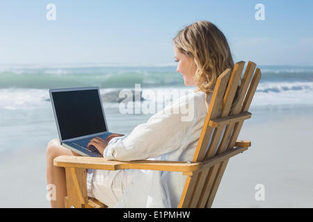 Una splendida bionda seduto sulla sedia a sdraio utilizzando laptop sulla spiaggia Foto Stock