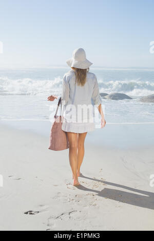 Donna bionda nel cappello che trasportano borsa da spiaggia affacciata sul mare Foto Stock