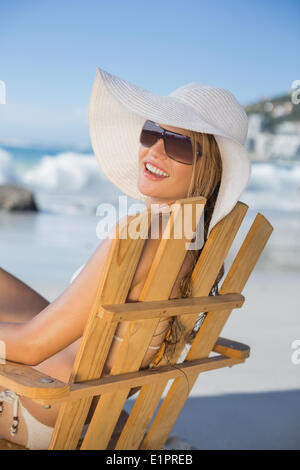 Donna sorridente nel cappello di paglia rilassante in sedia a sdraio sulla spiaggia Foto Stock