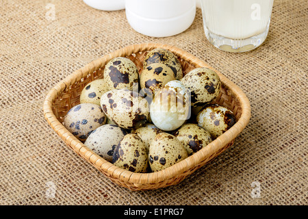 Uova di quaglia in un cestello di rattan, un bicchiere e una bottiglia di latte su una tovaglia di tela Foto Stock