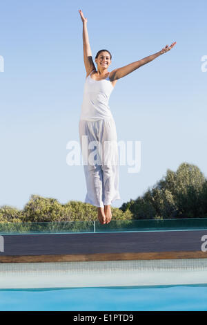 Happy brunette saltando a bordo piscina con bracci sollevati Foto Stock