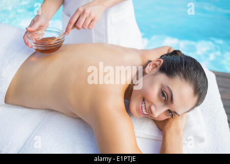 Sorridente brunette ottenere un miele trattamento di bellezza a bordo piscina Foto Stock