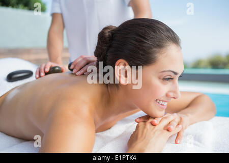 Happy brunette ottenendo un massaggio hot stone a bordo piscina Foto Stock