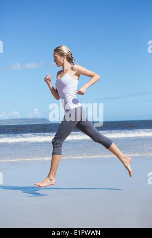 Montare focalizzato bionda jogging sulla spiaggia a piedi nudi Foto Stock