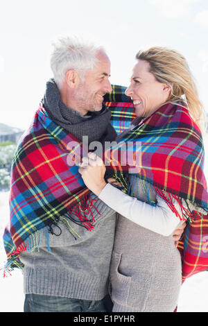 Coppia felice avvolto in una coperta permanente sulla spiaggia Foto Stock
