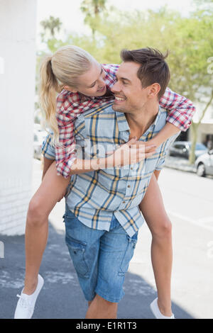 Giovane Hip uomo dando la sua ragazza bionda una piggy back Foto Stock