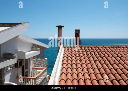 Vista sul mare e il tetto di tegole con camini dalla finestra dell'hotel in Sutomore, Montenegro. Foto Stock